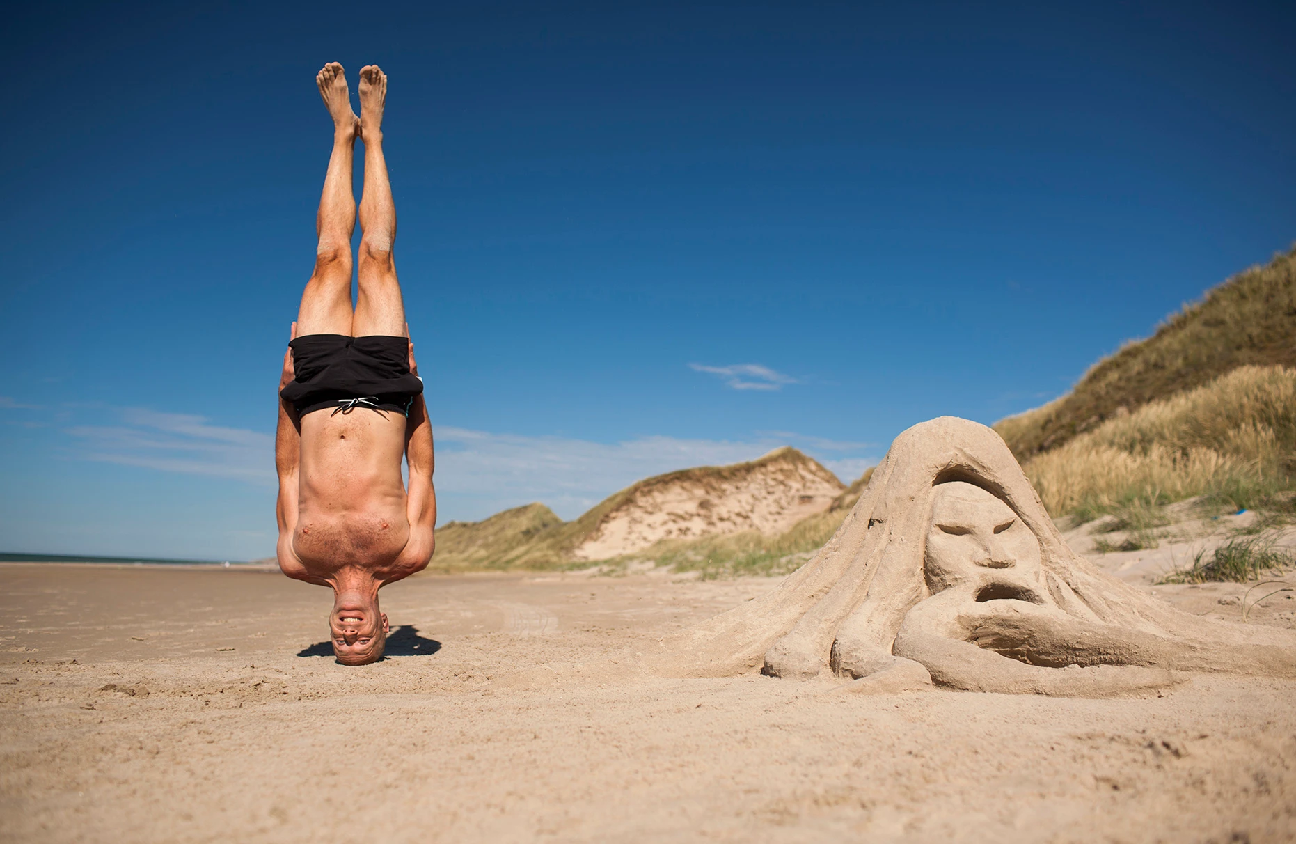 Mann in Badehose steht auf Kopf am Strand von Skiveren Nordsee-Seite in Dänemark