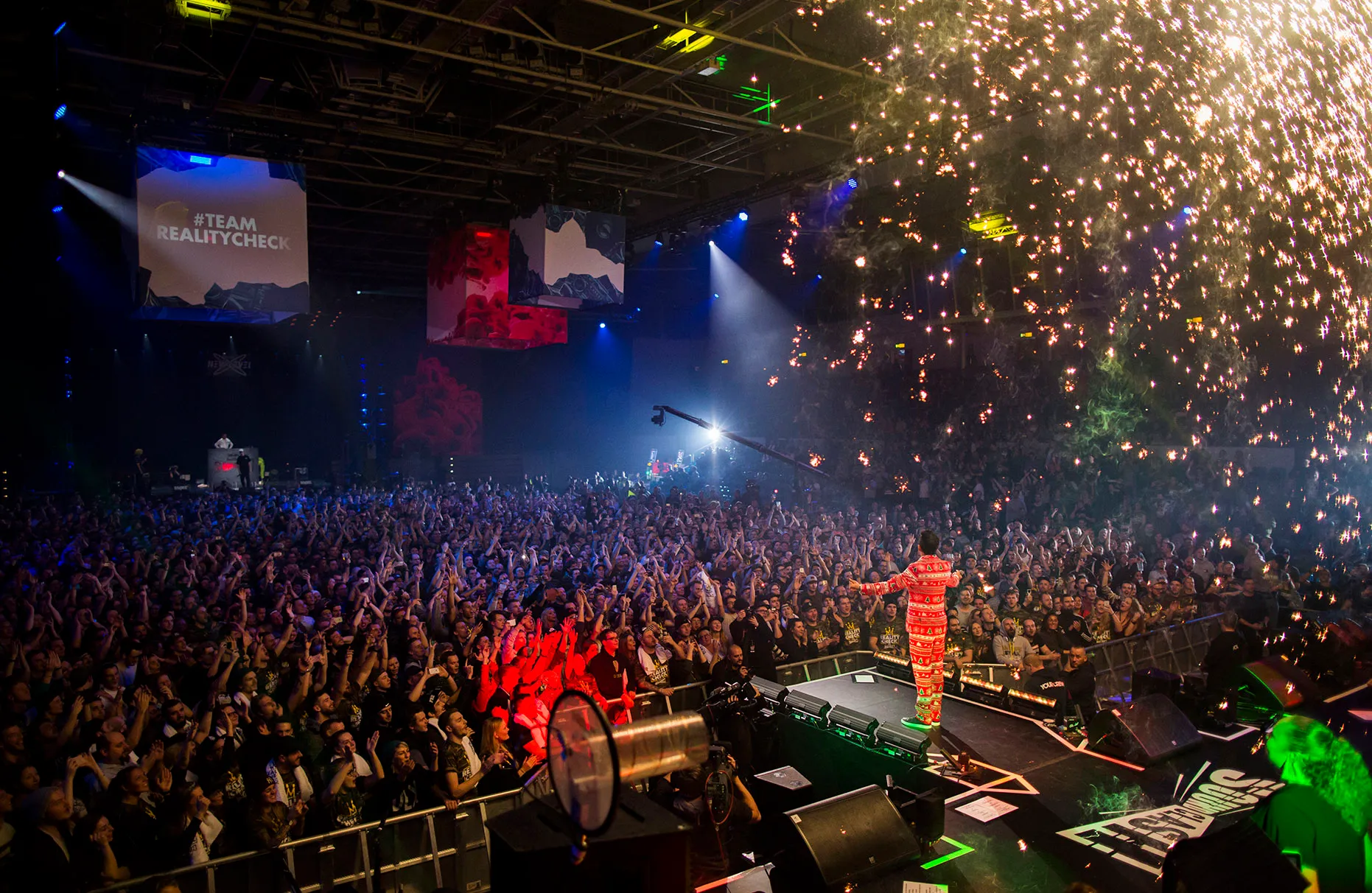 Eko Fresh vom Team Reality Check steht und singt auf der Bühne des Red Bull Sound Clash in Hamburg mit jubelndem Publikum im Hintergrund. Es regnet kupferfarbene Funken von der Pyrotechnik.