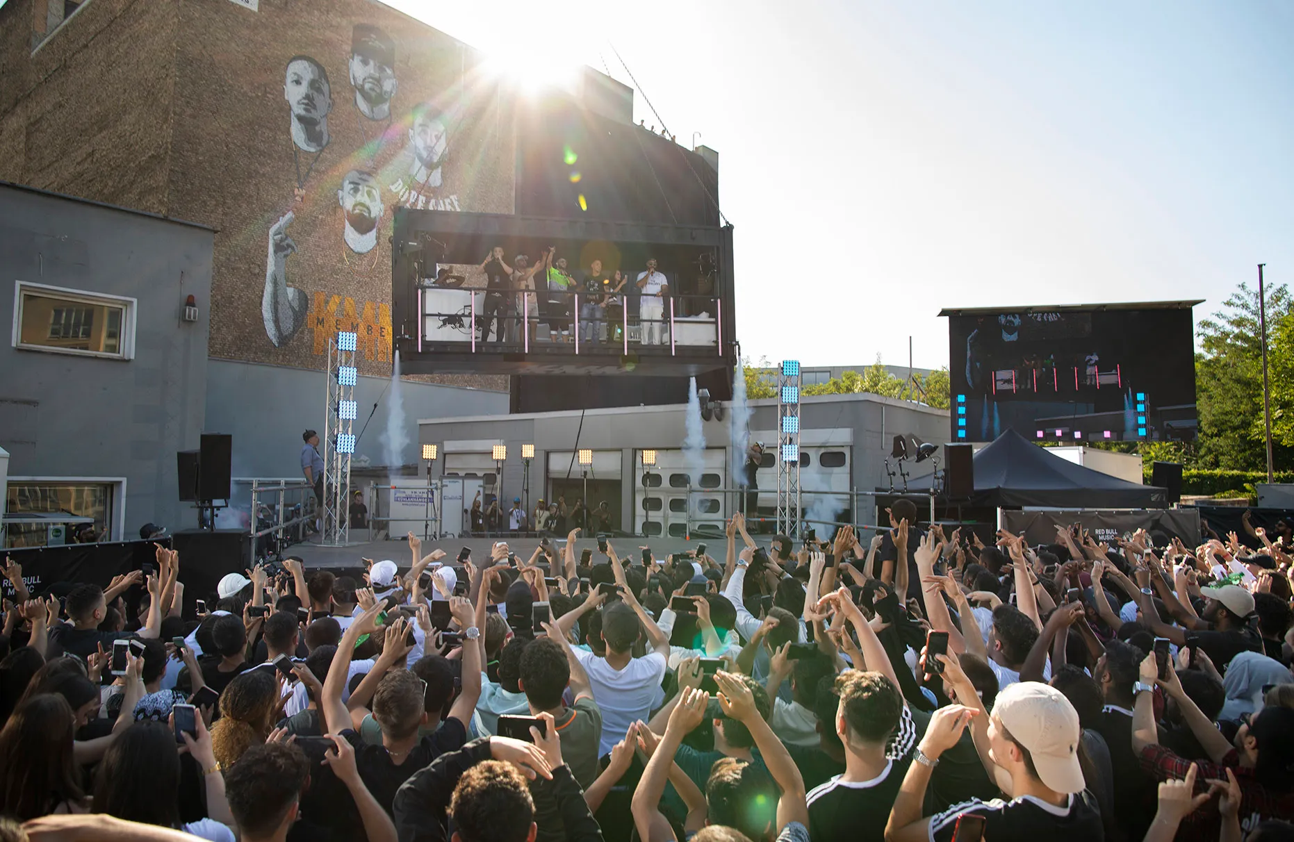 Die deutsche Band KMN-GANG singt und spielt in einem umgebauten Container, der an einem Schwerlastkran hängt. Das Publikum jubelt der Band von einem altberliner Hof- Gelände zu. Die Veranstaltung wurde von Red Bull durchgeführt.
