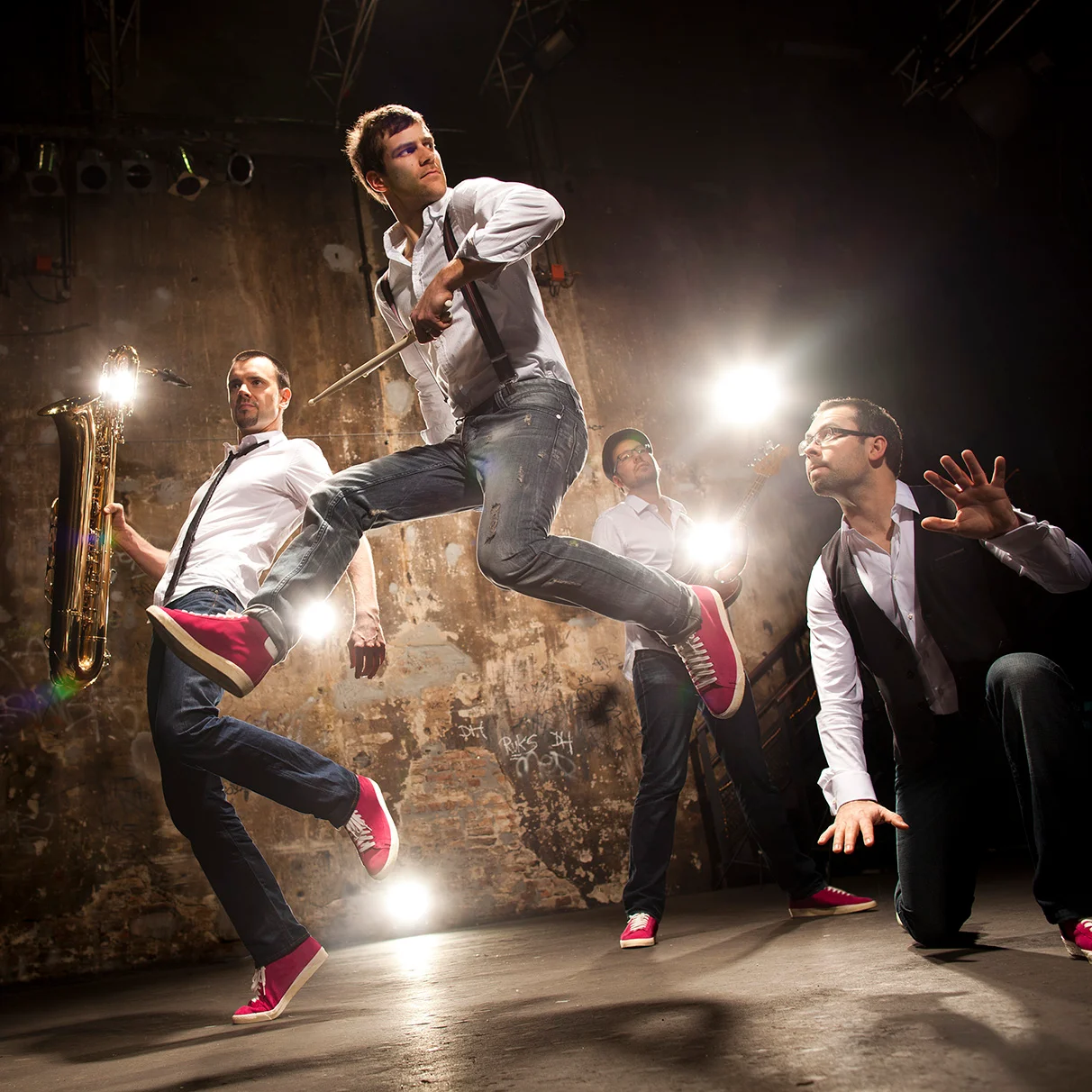 die Jazz- Band Mo Blow posiert und springt vor einer bröckeliegen alten Wand mit viel Gegenlicht in die Luft und hält dabei Musikinstrumenet in den Händen