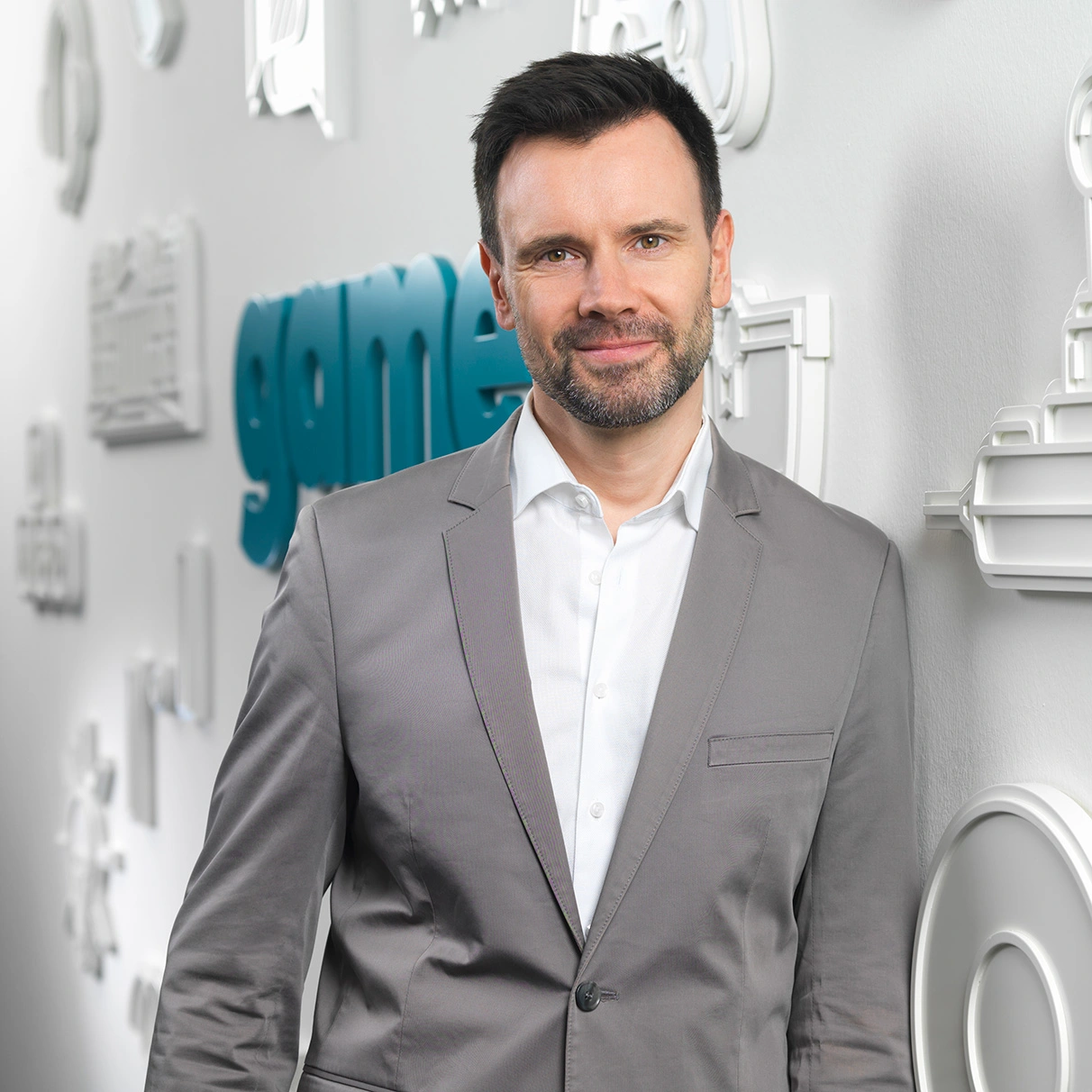 Felix Falk, CEO von game.de, posiert mit grauem Jacket und Hemd vor einer flüchtenden Wand, auf der das GAME Logo zu sehen ist. Prodziert für den Kunden game.e.V. mit Hasselblad 501c CFV 16