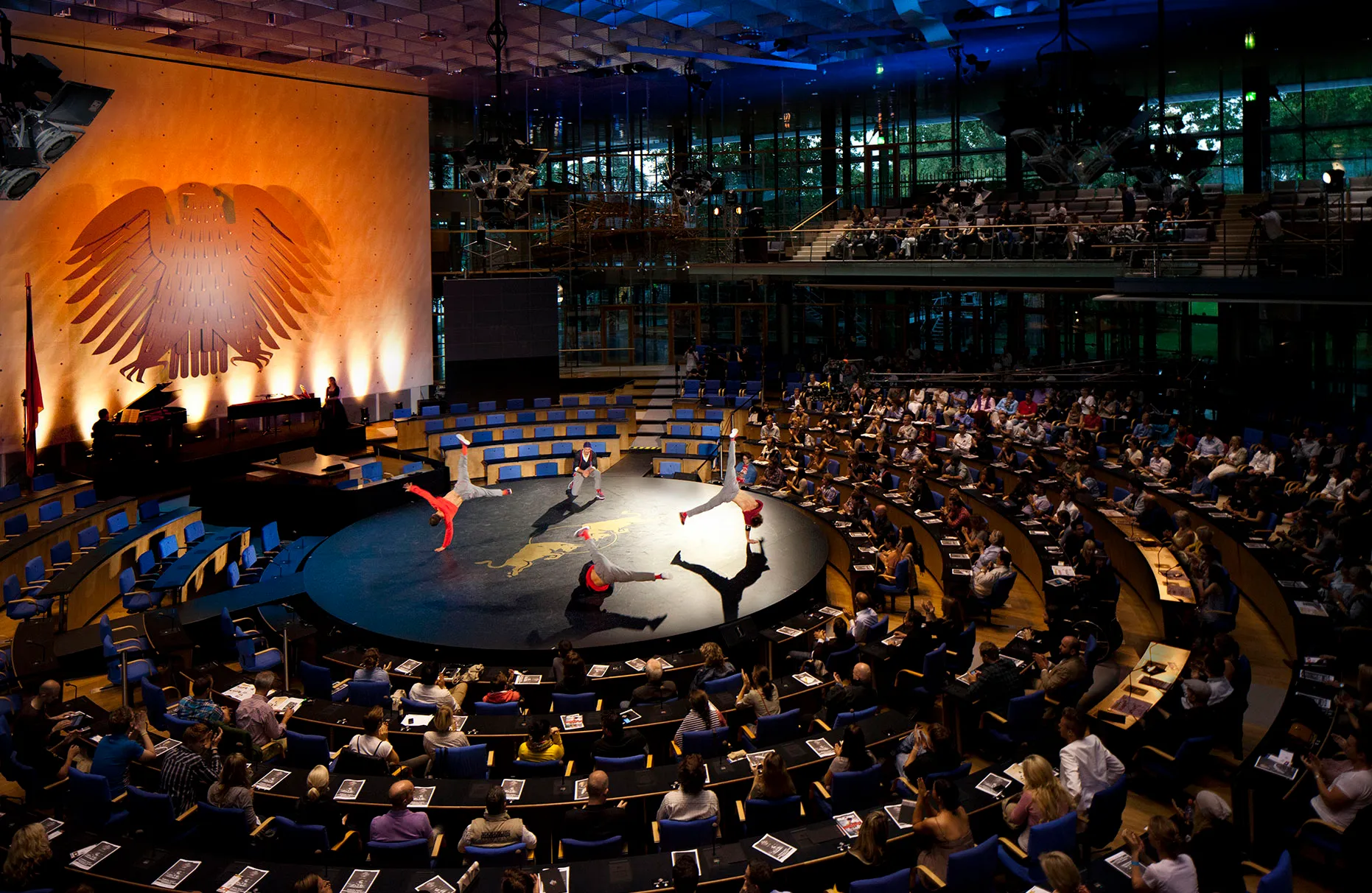 Die breakdance crew Flying Steps in Aktion während einer Flying Bach Vorführung im alten Bundestag in Bonn vor Publikum in den Sitzen. Aufnahme leicht von oben mit weitwinkliger Sicht auf Bundestag mit Adler. Prodziert für Red Bull.