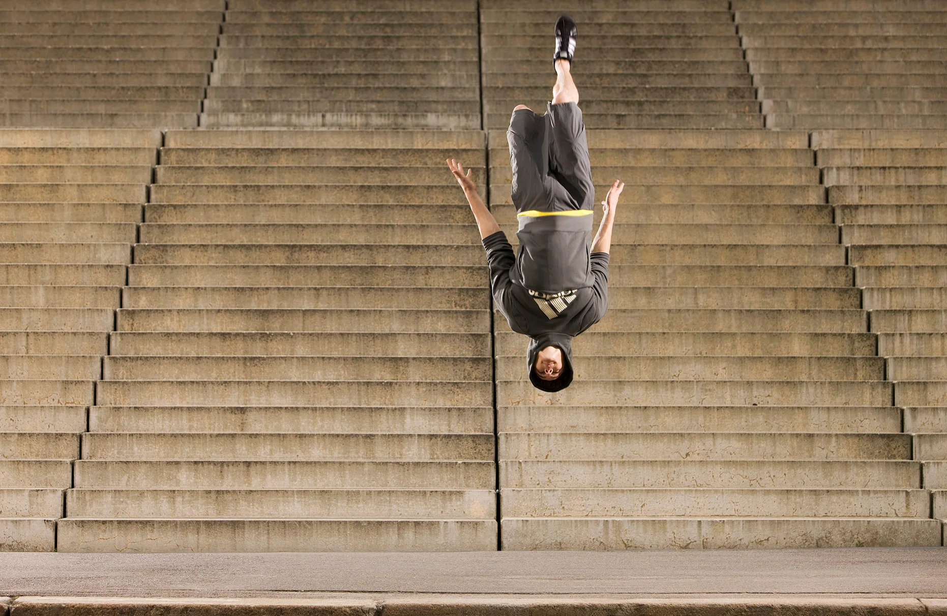 Der Akrobat und freerunner John Förtsre springt vor einer formatfüllenden Beton-Treppe einen Salto in sportlichem Adidas outfit. Prodziert für das adidas global lookbook/ Men's Training Spring Summer.