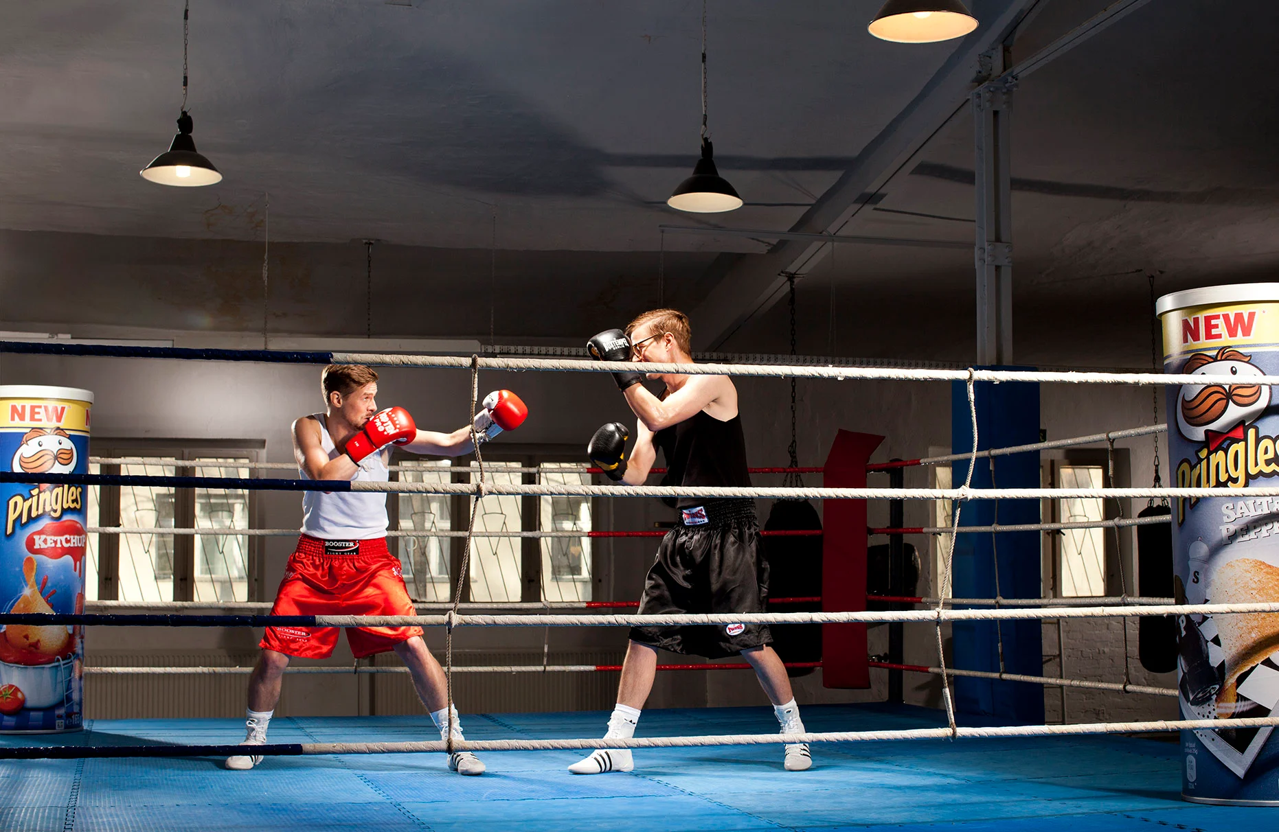 Joko Winterscheid und Klaas Heufer Umlauf stehen sich in Box outfit in einem Boxring zusammen mit je einer übergrossen Pringles Dose gegenüber. Gedämpftes Licht im Boxclub. Prodziert anlässlich einer Pringles PR Kampagne für Schröder & Schömbs PR.