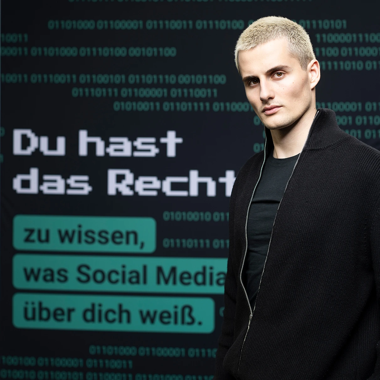 Luis Freitag von den elevator boys steht mit Blick in die Kamera vor einer Leinwand mit einer Grafik und dem Spruch: Du hast das Recht zu wissen, was social media über Dich weiss. Prodziert für eine Kampagne der NGO Hate Aid.