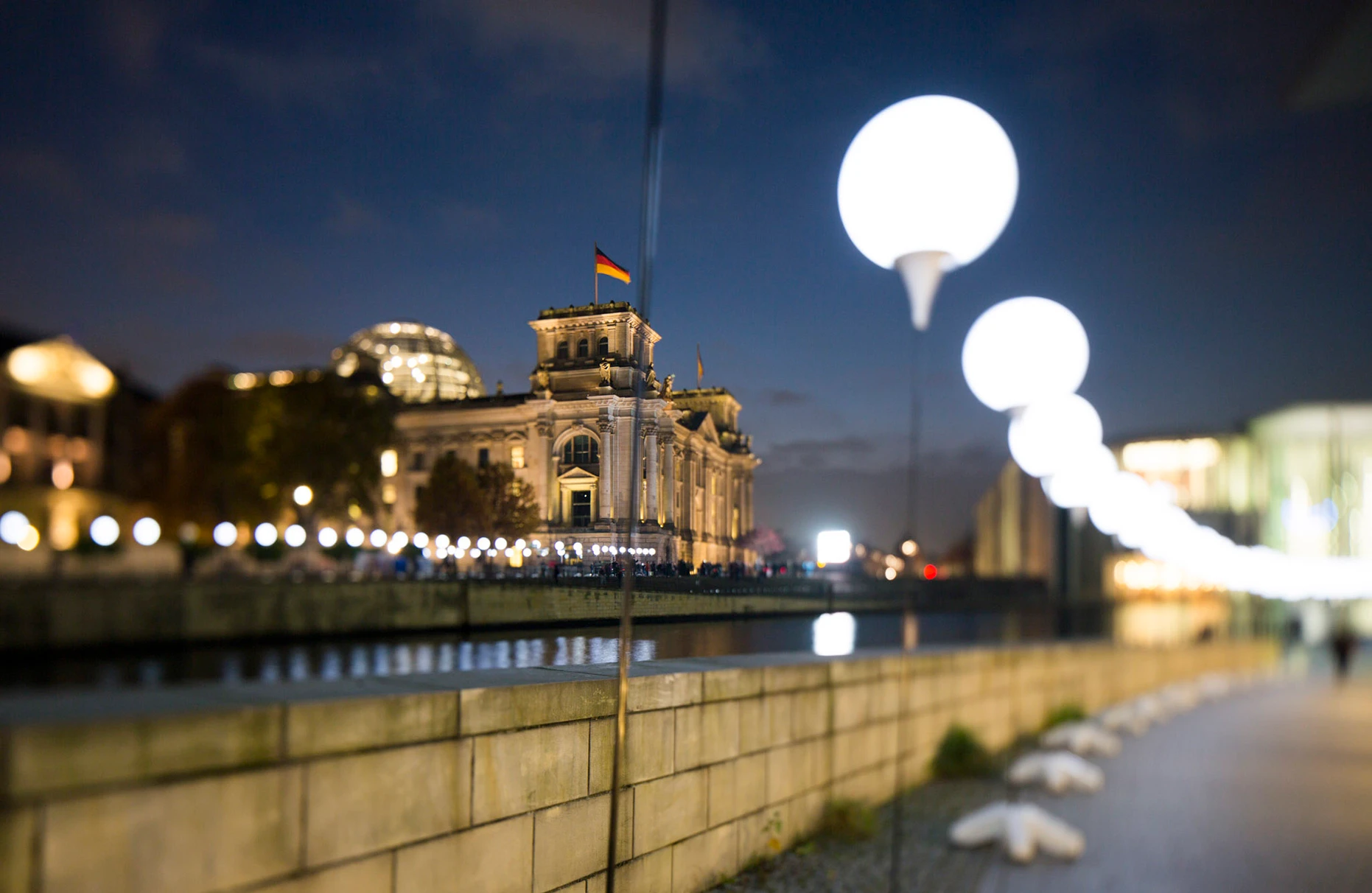 Zu sehen der Reichstag am Abend mit Spree. Anlässlich der 25 Jahre Mauerfall Feier stehen auf beiden Seiten der Spree Licht- Ballons, die zu einer langen Kette entlang der ehehmaligen Mauer gehören. Produziert für Visit Berlin Tourismus & Kongress GmbH