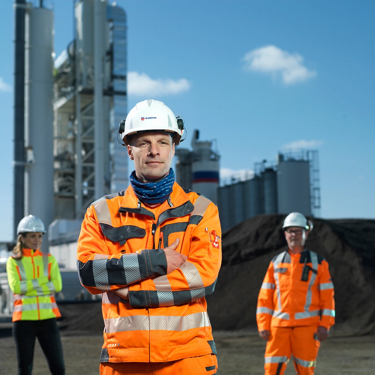 Drei Mitarbeiter des Asphalt Mischwerks Schönerlinde posieren vor dem Mischwerk bei blauen Himmel und Sonnenschein. Produziert für Eurovia Asphalt Mischwerk Schönerlinde mit Hasselblad 501c CFV 16.