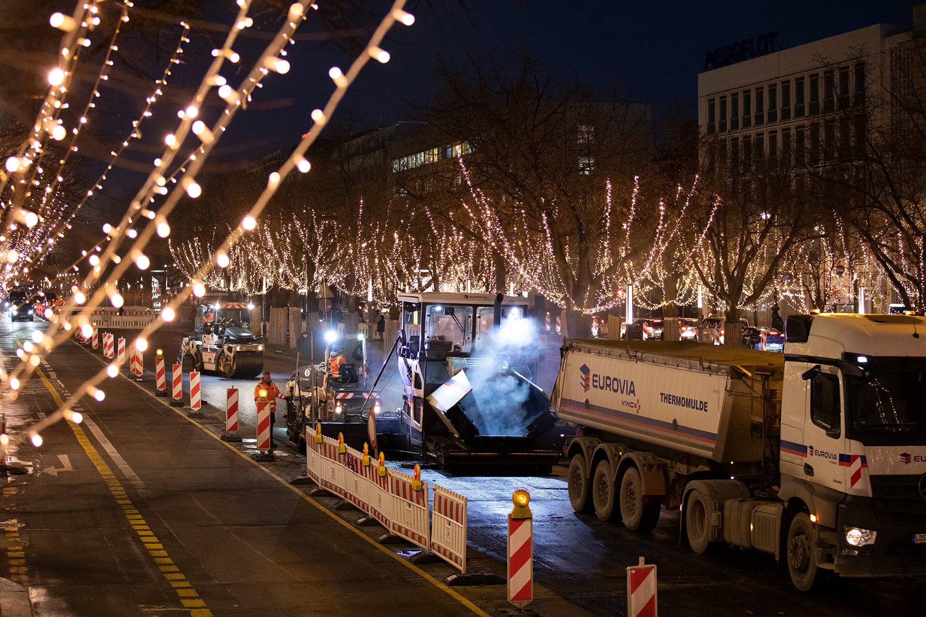 Ein Asphalt- Fertiger, Walze und Asphalt- LKW während einer Fahrbahn- Sanierung in der bekannten Strasse Unter den Linden. Abendliche Stimmung und die ganze Strasse Unter den Linden ist weihnachtlich festlich beleuchtet. Produziert für Eurovia Vinci.