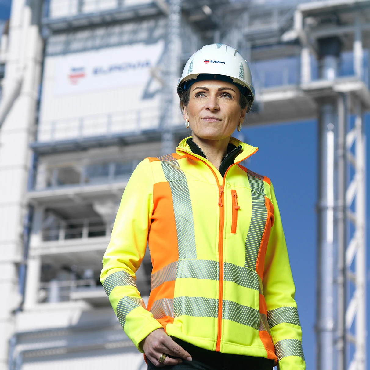 Katharina Siegel steht in PSA-Kleidung vor dem Asphalt Mischwerk Schönerlinde bei Sonnenschein. Produziert für Asphalt Mischwerk Schönerlinde mit Hasselblad 501c CFV 16.