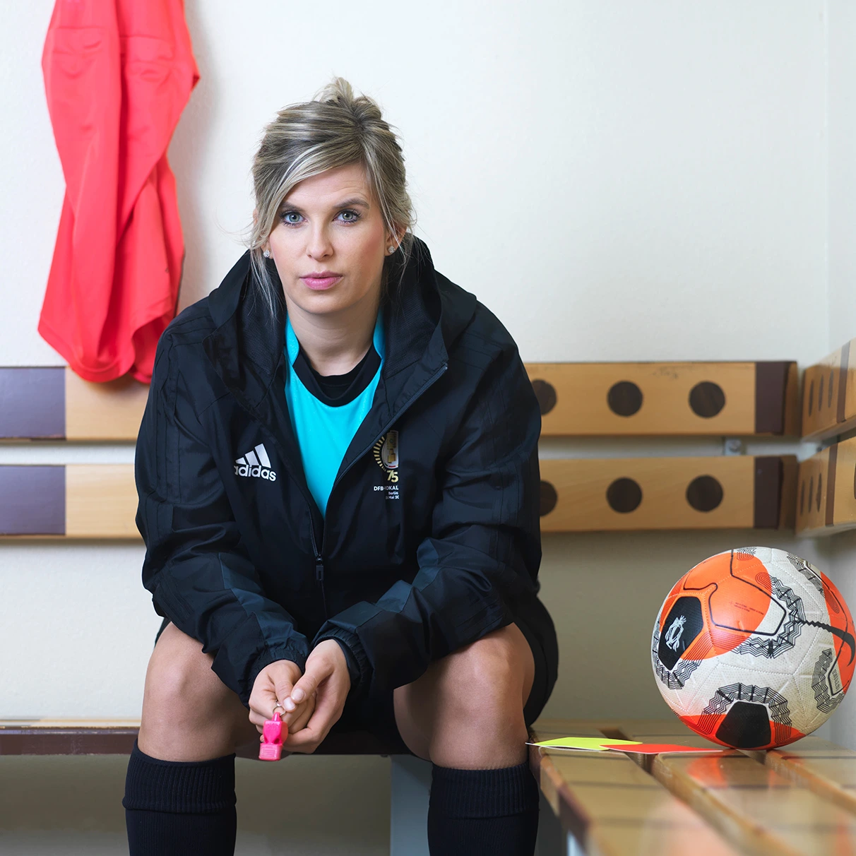 in einem Umkleideraum für Sportler sitzt die Fussball- Schiedsrichterin Franziska Koch auf einer Bank in Sport outfit und Schiedsrichterpfeife. Sie schaut sicher in die Kamera. Produziert für Runners World Magazin mit Hasselblad 501c CFV 16.