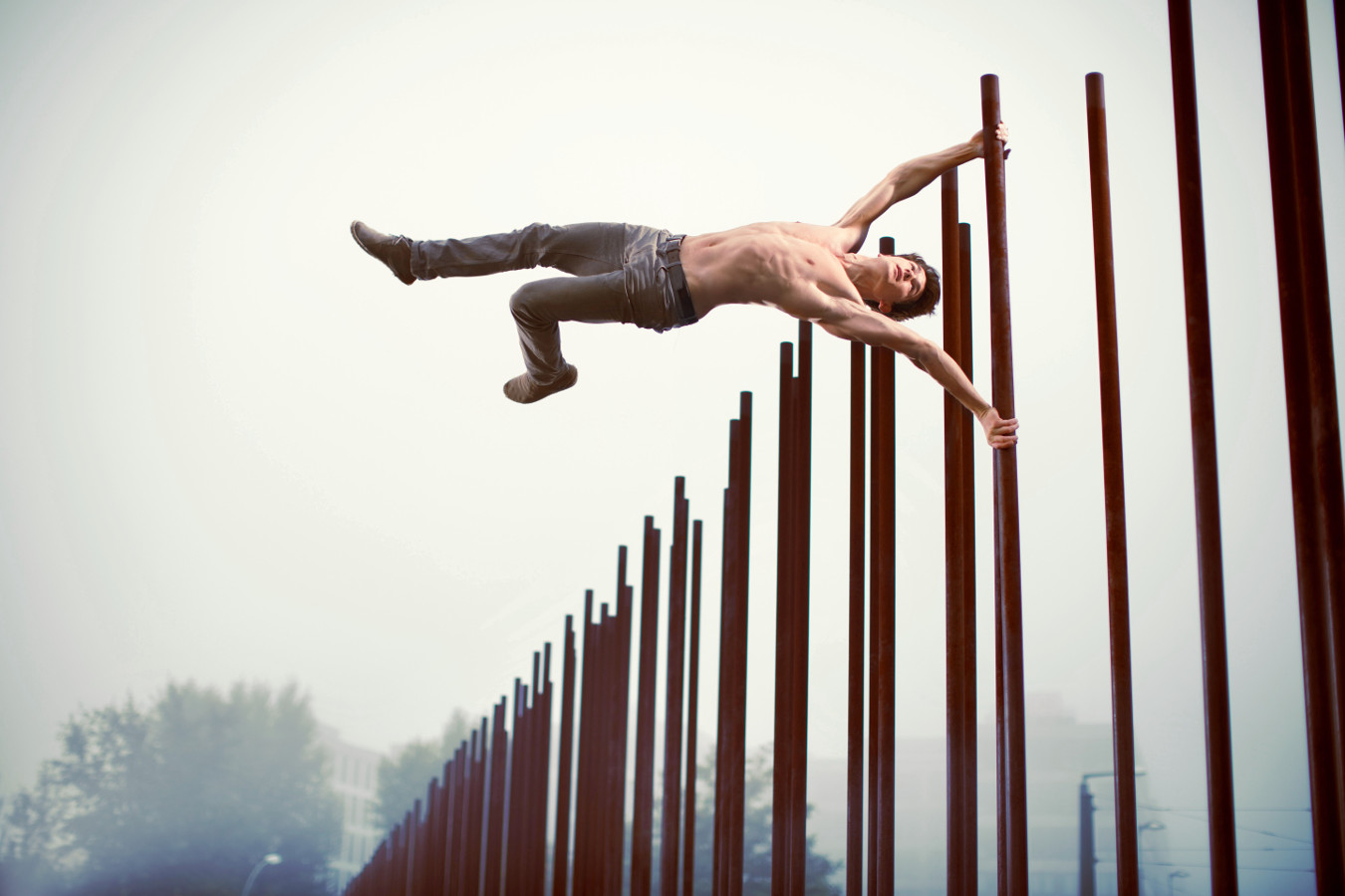 John Förster hält eine perfekte Human-Flag horizontal an den rostigen Stahlstelen der Gedenkstätte Berliner Mauer, Bernauer Straße in Berlin – Sport- und Konzeptfotografie, 100% real ohne Bildbearbeitung.