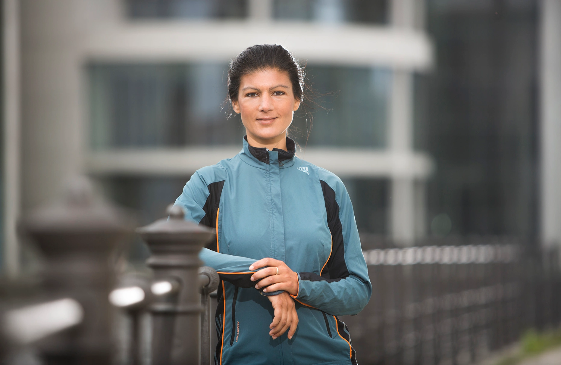 Die Politikerin Sarah Wagenknecht posiert an einem Geländer an der Spree vor dem Reichstag in Sport outfit. Produziert für Runners World Magazin.