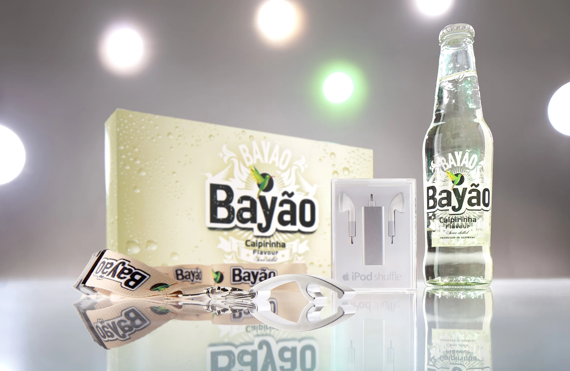 Eine Bayao Caipirinha Flasche steht zusammen mit Karton, ipod und Flaschenöffner-Band auf weisser Plexiplatte vor hellem Studiohintergund mit inszenierter Gegenlichtbeleuchtung. Produziert für die PR-Agentur Schröder und Schömbs PR aus Berlin.