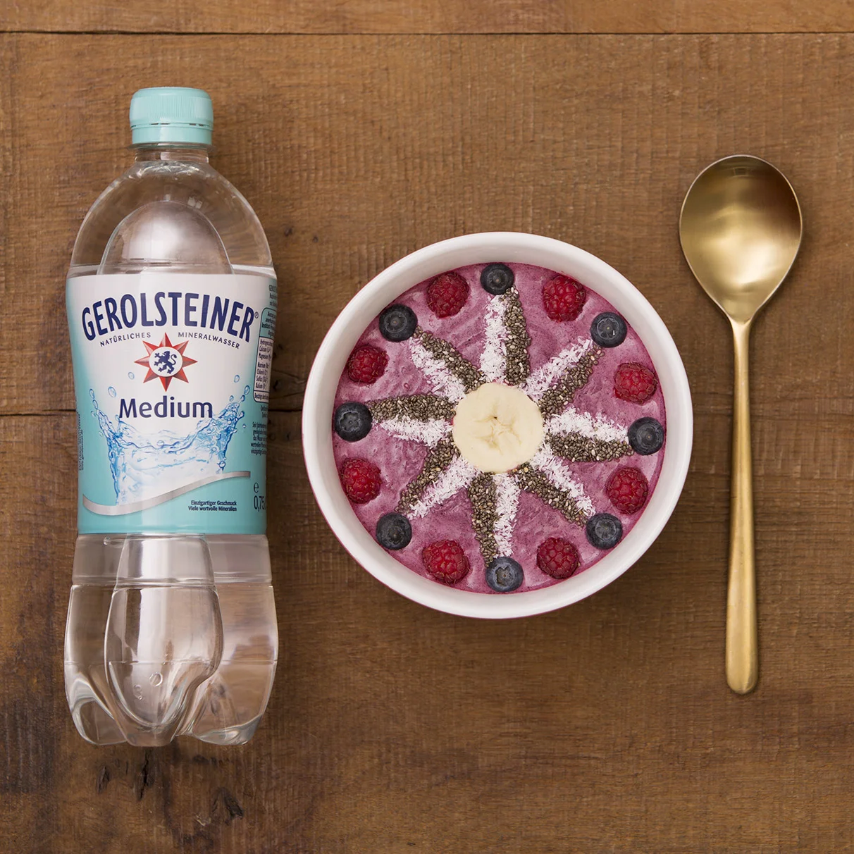 Auf einem natürlichen Holzuntergrund liegt eine Gerolsteiner PET Flasche mit gefüllter Müsli Schale und goldenen Löffel. Das topping in der Müslischale ist aufwendig zu ene Stern gelegt, der den Gerolsteiner Stern nachahmen soll. Das ganze ist von oben im flat lay Stil fotografiert . Produziert für die PR-Agentur Schröder und Schömbs PR aus Berlin.