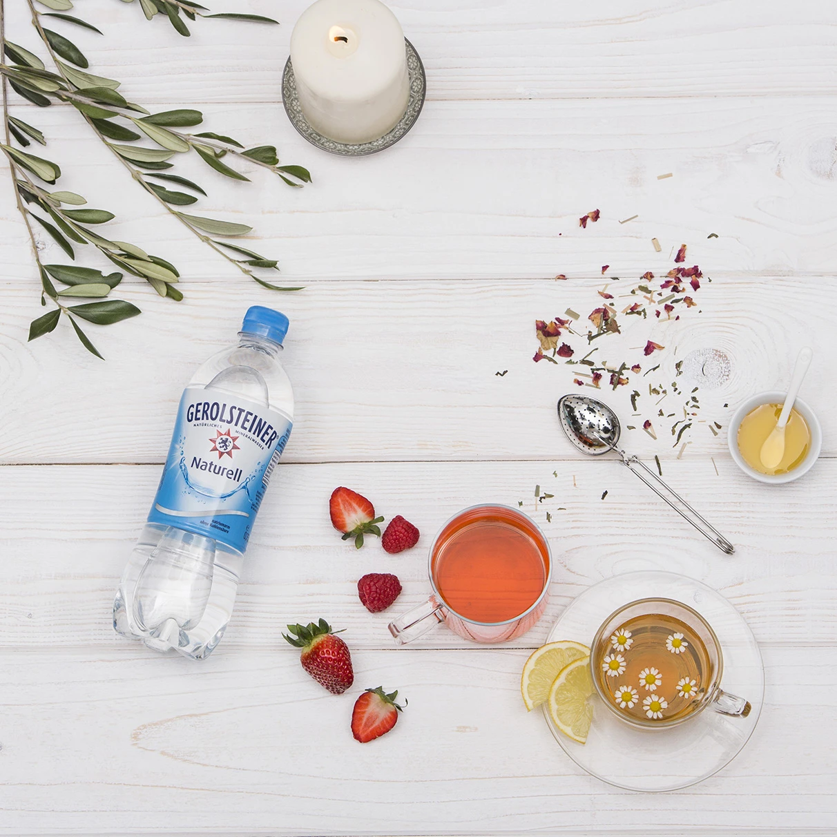 Auf einem weissen Holztisch liegt lose und ungeordnet eine Gerolsteiner PET Flasche, Obst und Tee mit gefüllten Tee Gläsren. Das ganze ist von oben im flat lay Stil fotografiert . Produziert für die PR-Agentur Schröder und Schömbs PR aus Berlin.
